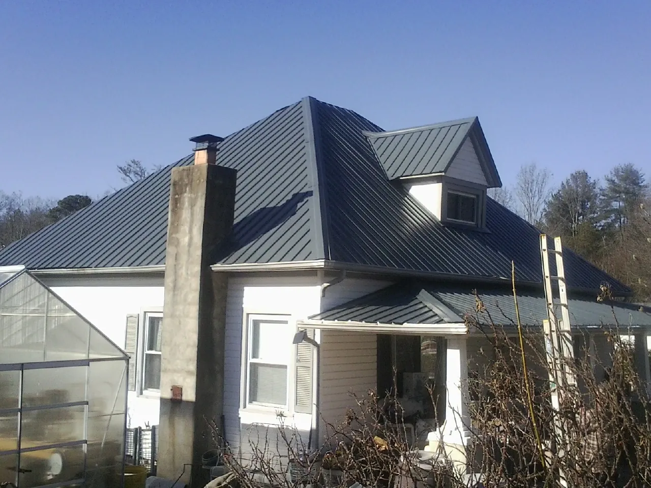 Dark blue standing seam metal roof on a white farmhouse with dormer — Slate & Tile Roof Repair by Roofing Brothers in Wilderville