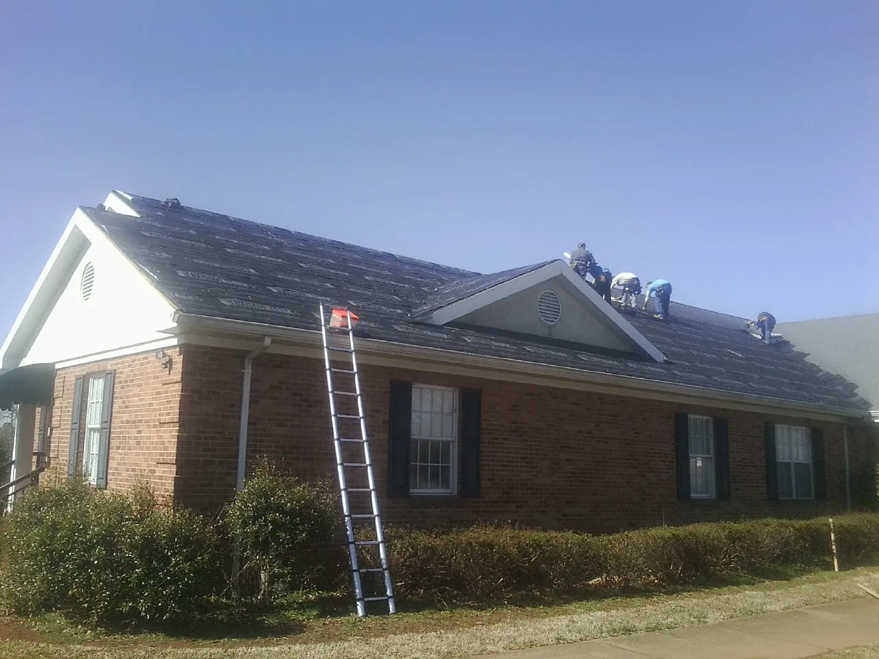 Crew tearing shingles off a brick ranch roof with a ladder set — Metal Roof Repair work by our crew in Wilderville