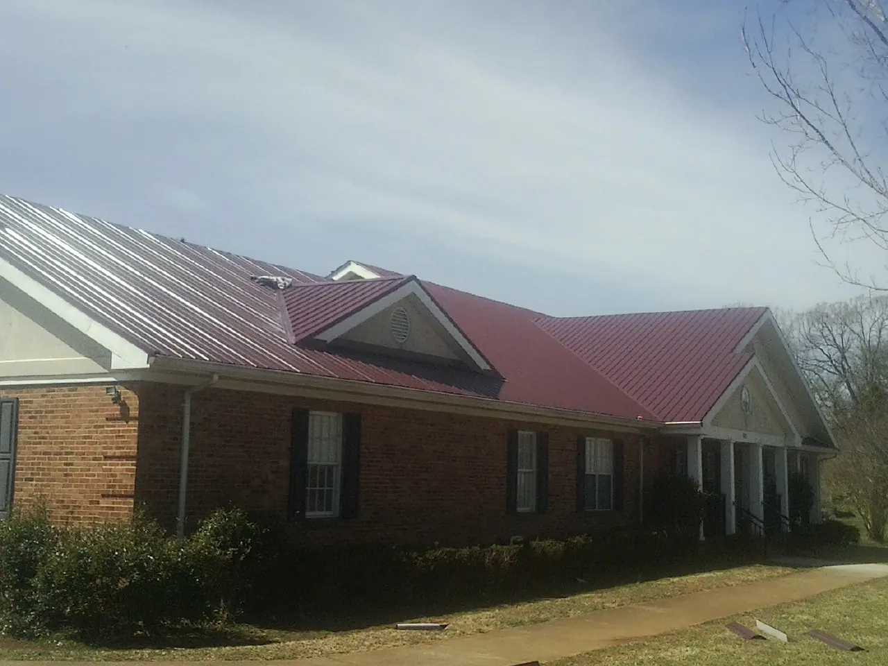 Red metal roof with gabled entries on a long brick building, from a Hail Damage Roof Repair job in Wilderville