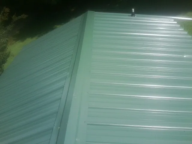New green metal panels meeting at the ridge of a roof — Flat Roof Repair work by our crew in Wilderville