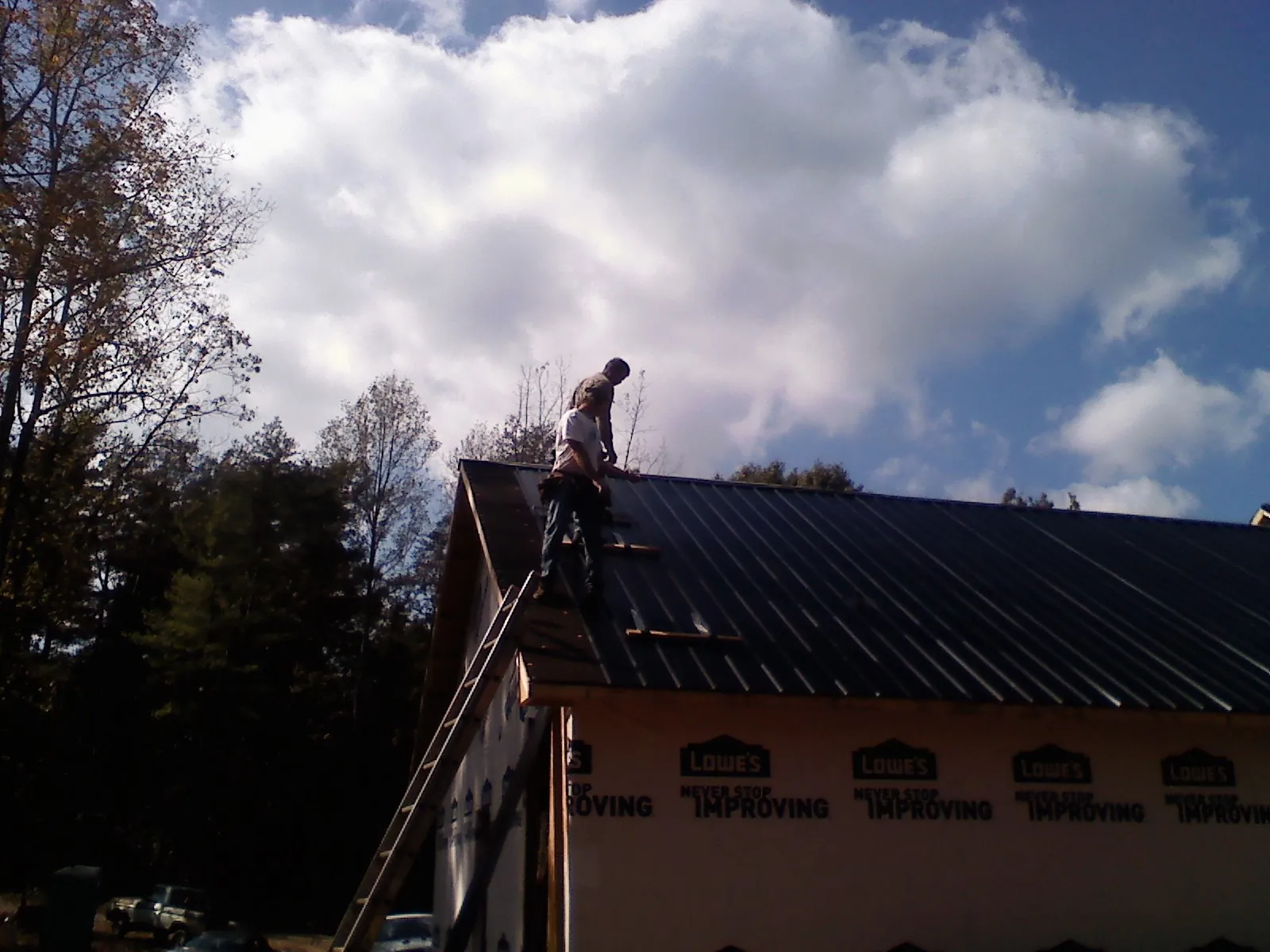 Roofer fastening dark metal panels high against a cloudy sky, from a Roof Inspection job in Wilderville